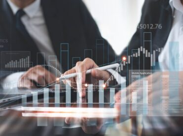 Scalable Procore Solutions A businessman utilizes Procore Scalable Solutions to increase revenue in his construction business. Image includes a white growth bar graph superimposed over two businesspeople at a desk.
