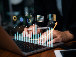 A tech image of an upward trending graph superimposed over an image of hands typing on a keyboard.