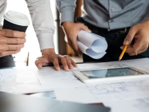Two workers lean over a tablet to examine Procore reporting tools.